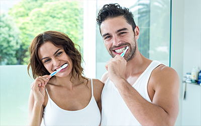 A man and a woman brushing their teeth together